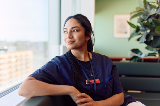 Thoughtful female medical worker looking out of window during work break