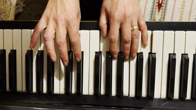 Top view of adult female hands playing gentle piece of classical music on black piano. Scene captures the movement, rhythm and elegance of performance, highlighting beauty of live instrumental play