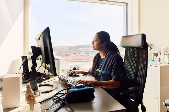 Focused female doctor working on computer during her shift while sitting at desk in clinic office