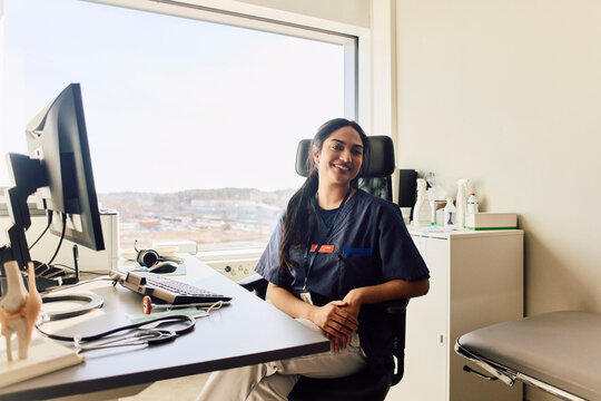 Portrait of smiling female clinician sitting confidently on chair in clinic office
