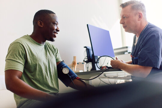 Male doctor having conversation with patient while checking blood pressure in clinic