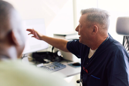 Male healthcare professional explaining medical reports to patient over computer screen