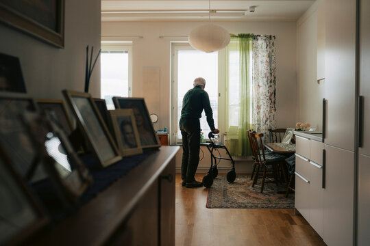 Full length of senior man standing near window with help of mobility walker at retirement home