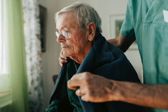Caregiver putting blanket on senior man at nursing home