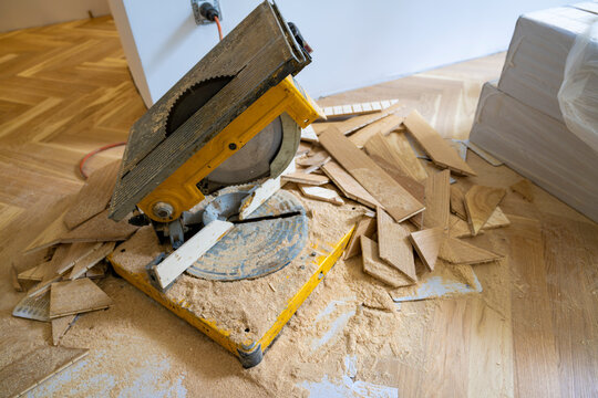Professional parquet flooring installation with miter saw, wood offcuts and sawdust during residential home renovation creating elegant herringbone hardwood floor