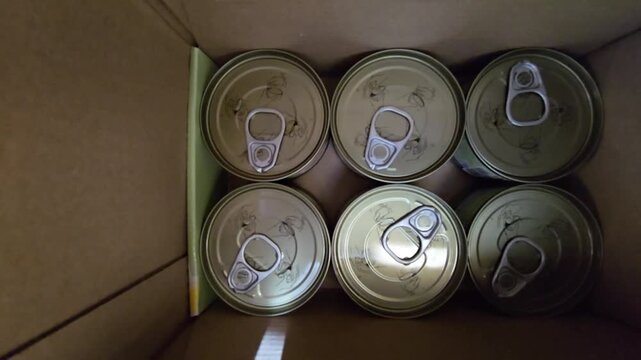 Top-down view of several sealed food cans with pull-tab lids inside a cardboard box.