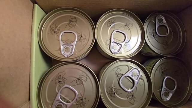 Top-down view of several sealed food cans with pull-tab lids inside a cardboard box.