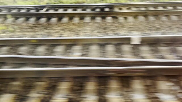 View from the window of fast moving train looking down at parallel railway tracks. The rails rush by creating a strong sense of speed and motion. Concept of transportation and travel. Slow motion