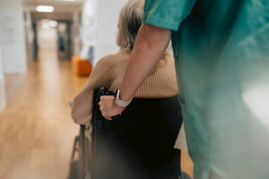 Midsection of female nurse pushing senior woman in wheelchair at elder care facility