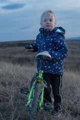 Little girl standing with her bright green bicycle in an open field, looking directly forward, capturing a moment of childhood exploration and nature connection © somemeans