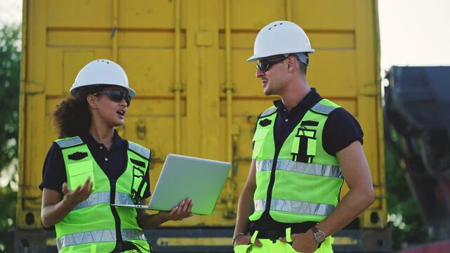 Logistics workers and engineers in safety vests using laptop while checking inventory at container terminal, representing industrial management, international trade, and supply chain technology.