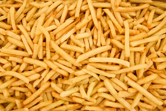 Full frame top-down view of a generous pile of golden crispy french fries on rustic wooden background, representing tasty fast food appetizer and catering buffet event.