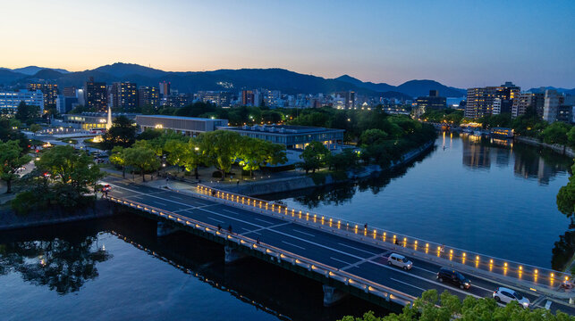 view of the motoyasu river with the illuminated peace bridge and the park at sunset during the blue hour
