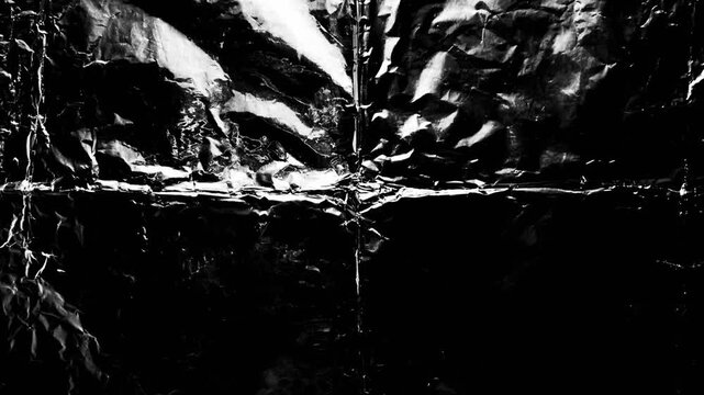 crumpled black metallic foil texture reflects harsh light creating dynamic abstract contrast
