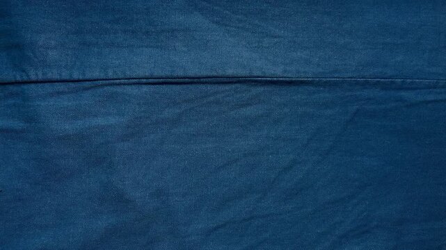 blue denim fabric texture reveals subtle creases along a horizontal stitched seam in a minimalist cinematic overhead view