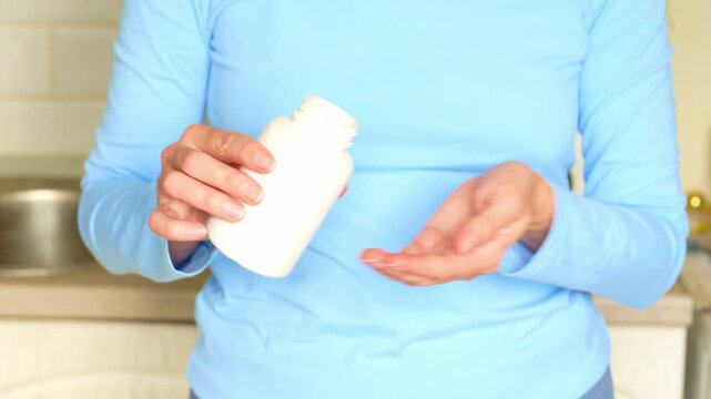 Woman hands receive golden fish oil capsule from white bottle. Daily wellness routine, omega 3 supplement capsule in woman hand. Healthy lifestyle.