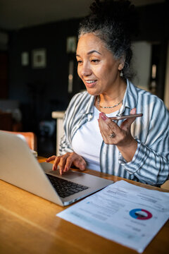 Mature woman managing finances at home with laptop and phone