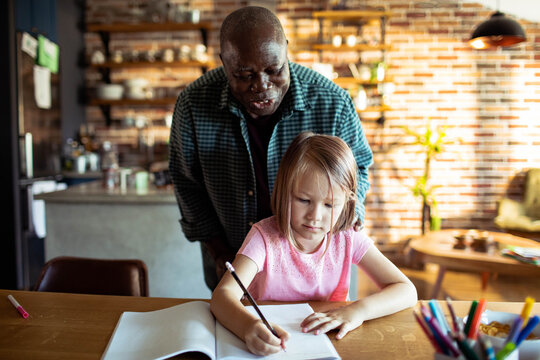 Adult helping girl with homework at kitchen table at home