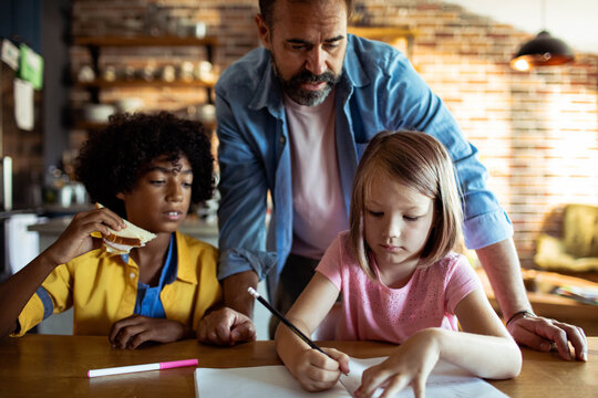 Father helping children with homework at kitchen table
