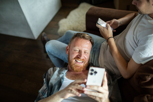 Two men relaxing at home on a couch with smartphones