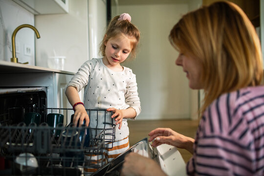 Parent and child loading dishwasher in home kitchen