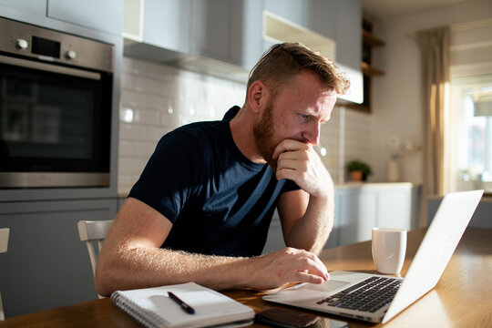 Focused man working on laptop in home kitchen