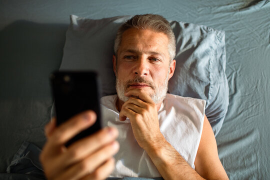 Middle-aged man using smartphone in bed at night
