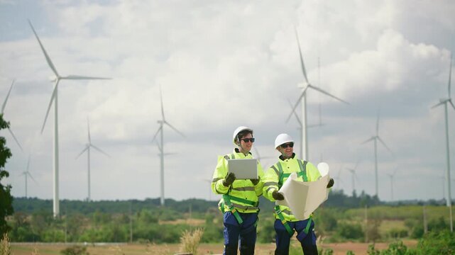 A professional Windmill engineer inspects and discusses operations at a wind turbine farm. Eco technology for electric, industry environment, sustainable technology wind power maintenance.
