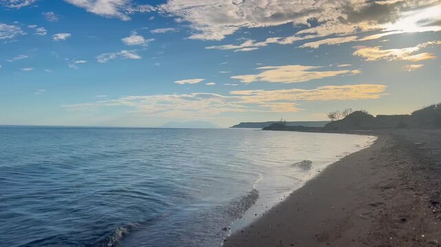 Cinematic view of a calm sea coast with small waves on sandy beach and distant island outline on a sunny afternoon in Edirne, Turkey.