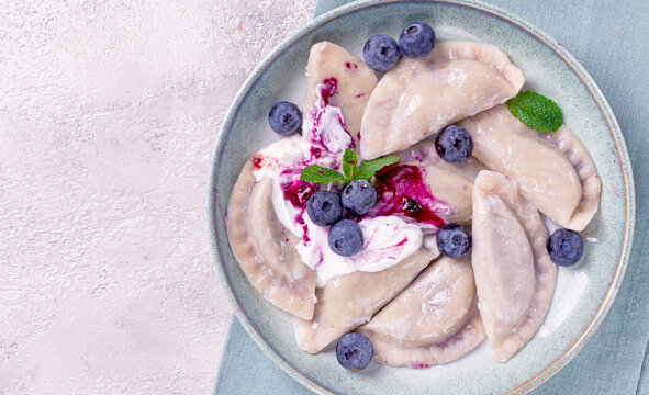 Delicious sweet dumplings served with blueberries and cream in a bowl on a teal napkin