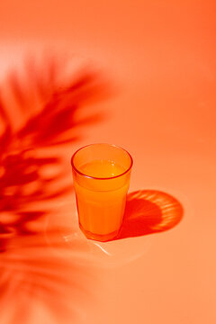 orange juice in a glass, on an orange background, shadows from leaves, harsh light, no people,