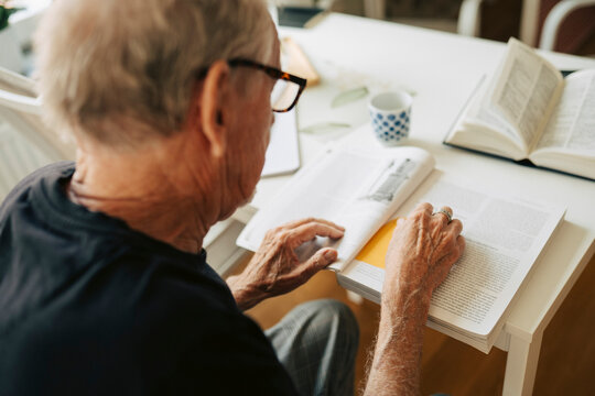 Over the shoulder view of senior man reading book while sitting at table