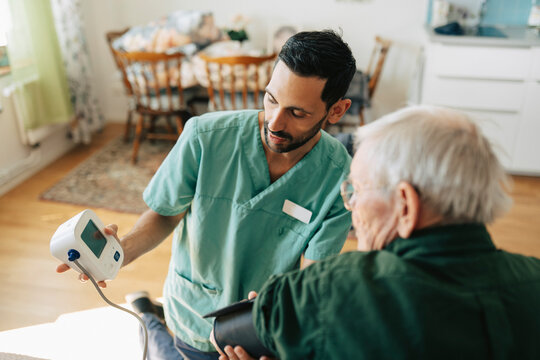 Male nurse checking blood pressure of senior man with digital monitor