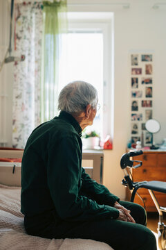 Side view of lonely man looking away while sitting on bed in nursing home