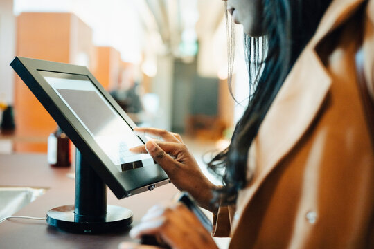 Close-up shot of female entrepreneur using touch screen kiosk at shared workspace front desk