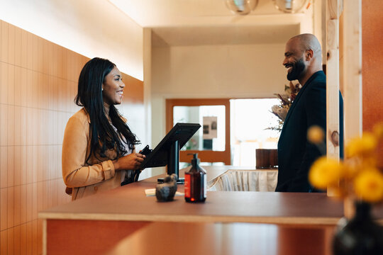 Happy female freelancer interacting with male receptionist while standing at shared workspace front desk