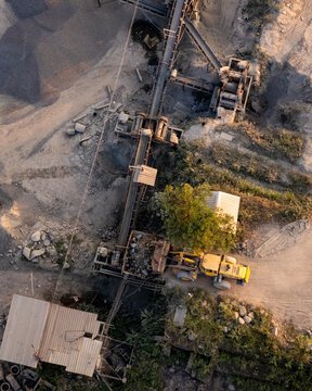 Aerial view of a mining site featuring conveyor belts transporting gravel and a yellow front-end loader operating on the ground in Indonesia.