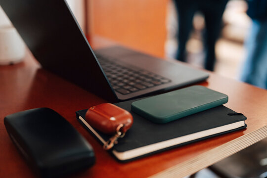 Close-up of smart phone in green case resting on black diary next to laptop at modern coworking space
