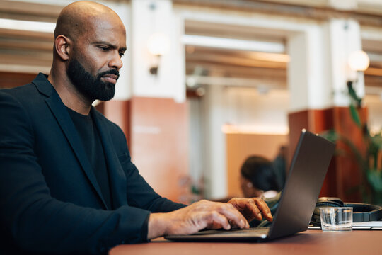 Focused businessman typing mail on his laptop while sitting and working at modern coworking space