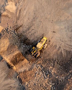 Aerial view of a yellow bulldozer working in a rocky quarry with piles of gravel and dirt, Indonesia.