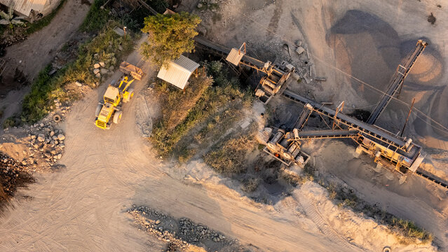 Aerial view of a yellow bulldozer operating near a stone crushing conveyor belt system in a quarry in Indonesia.