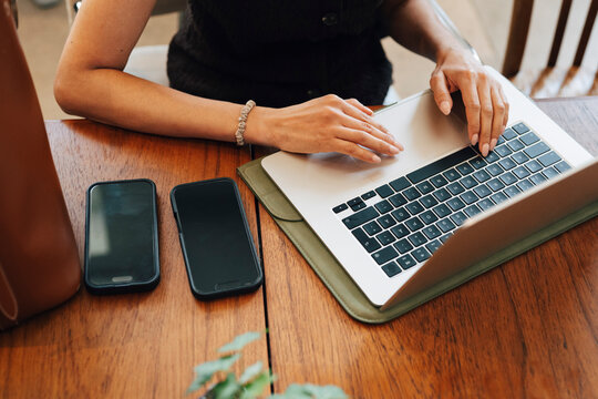 High angle view of female freelancer working on laptop while sitting at desk with two smart phones in coworking office