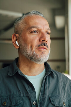 Thoughtful male entrepreneur with wireless earbuds at workspace