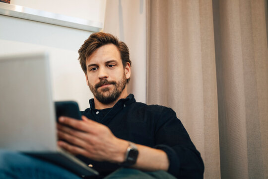 Low angle view of male freelancer using smart phone during his work session at coworking space