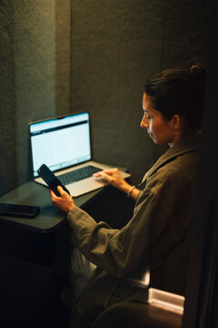 Businesswoman checking her smart phone during her work session while sitting inside office cubicle