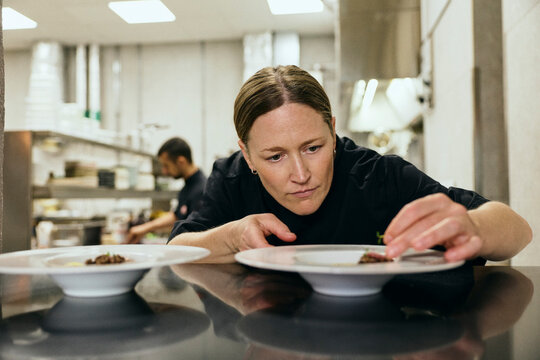 Focused female chef adding final details to dish before serving