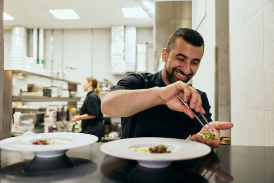 Smiling male chef adding final touches to dishes while working in restaurant kitchen
