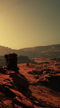 The scene shows a vast desert landscape with rocky formations under a setting sun. Shadows stretch across the ground as the day ends. The colors shift from warm to cooler tones in the sky.