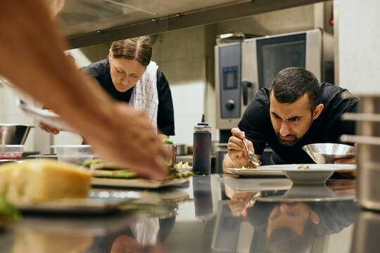Male and female professional kitchen staff preparing fine dining plates for customers