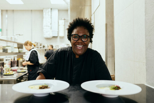 Portrait of happy female chef with ready to serve dishes on kitchen pass window